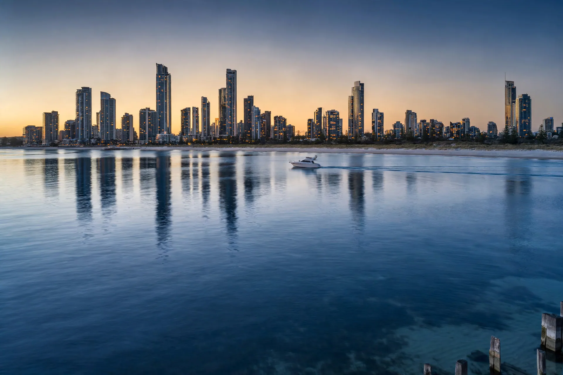 A yacht on calm water with a high-rise skyline behind at dusk