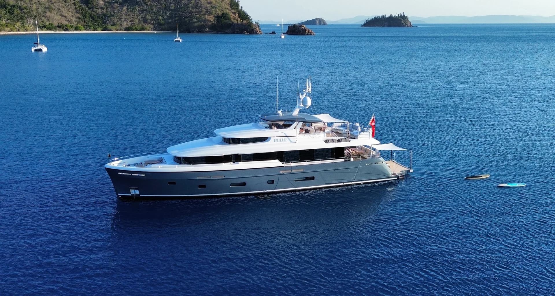 BELLE at anchor in blue water with paddleboards beside the stern