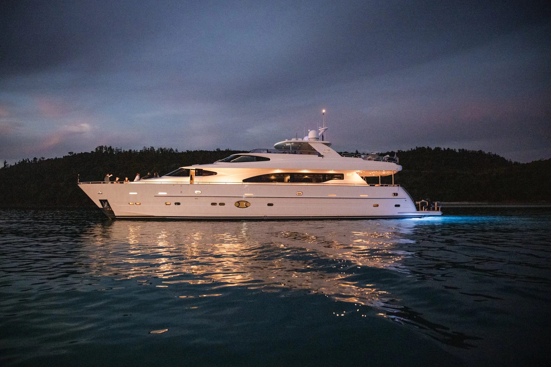 Encore illuminated at anchor at dusk with underwater lights visible.