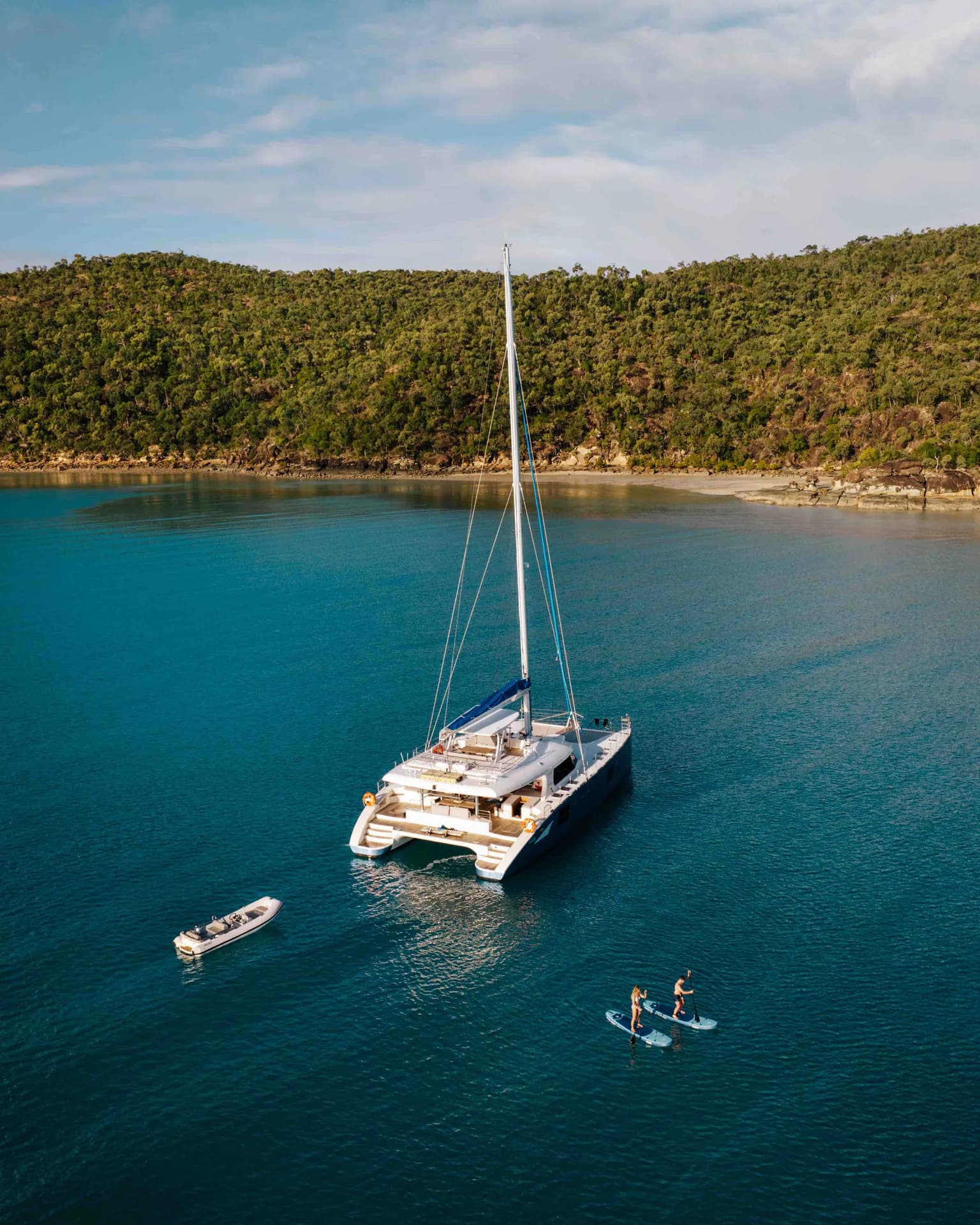Feng anchored in a tropical bay with a tender off the stern and forested hills behind.