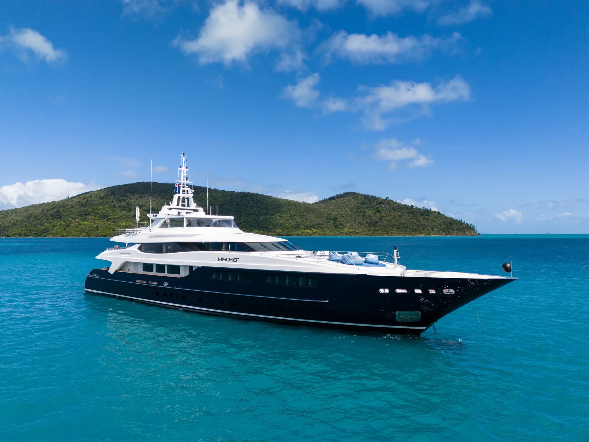 Mischief anchored in bright turquoise water with hills in the background